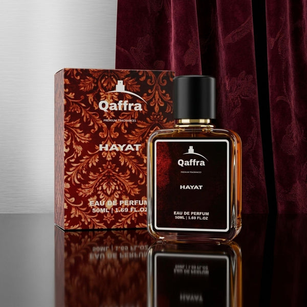 A bottle of Qaffra Hayat 50ml Eau de Parfum with its ornate red and gold patterned box, displayed on a reflective black surface with a dark maroon velvet curtain background.