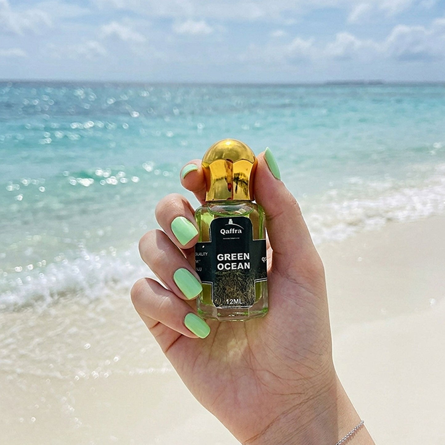 Hand holding a bottle Attar labeled 'Green Ocean' against a beach backdrop